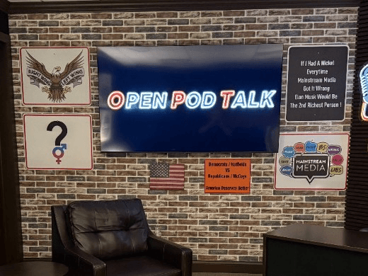 The Open Pod Talk screen glowing on the studio's brick wall above a leather guest chair